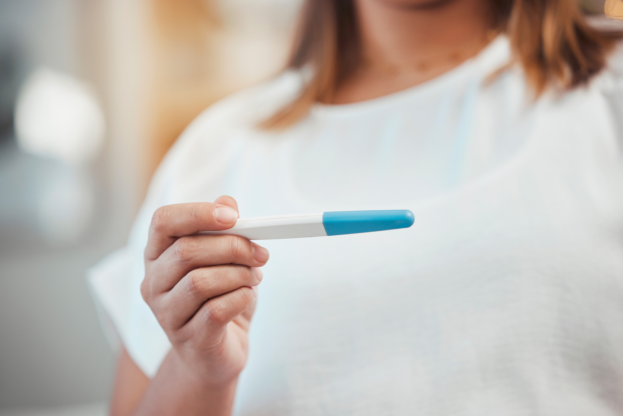 Image of a white woman with blonde hair holding a white and blue pregnancy test.