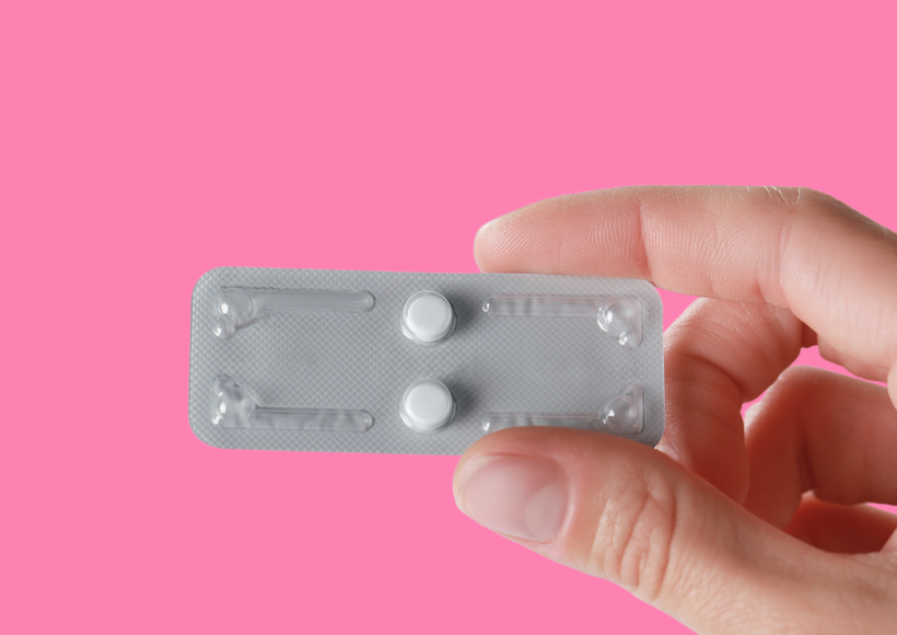pink background with white complected hand holding two Plan B emergency contraception pills