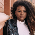 Image of a young beautiful African American woman leaning against a brick wall contemplating how to tell her parents she's pregnant. This image is the header image for the Problem Pregnancy Center.